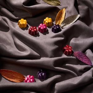 Луксозни шоколадови бонбони, подредени върху сатен с декоративни листа – елегантна визия на подаръчен комплект.