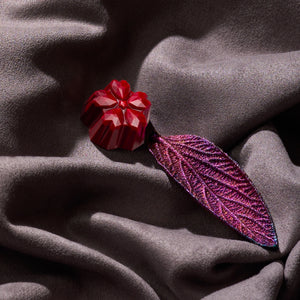 Червен шоколадов бонбон във форма на цвете до лилаво декоративно листо върху сатен – детайлна продуктова снимка