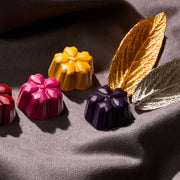 Асортимент от цветни шоколадови бонбони (розов, жълт и лилав) с метални листа – луксозни ръчно изработени бонбони.