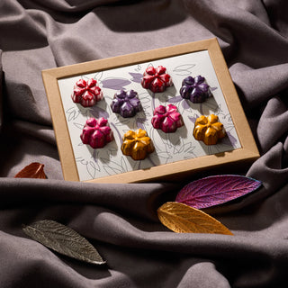 Подаръчна кутия с луксозни шоколадови бонбони във форма на цветя (червени, розови, лилави и златни) върху сатенен фон